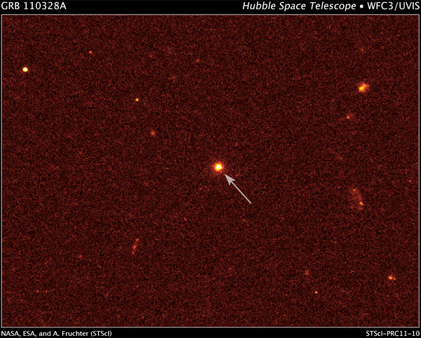 Рис. 3. Небольшая галактика (отмечена стрелкой) в 3,8 миллиардах световых лет от Солнца — предполагаемый источник всплеска GRB 110328A. Снимок сделан в видимом свете 4 апреля 2011 года широкоугольной камерой телескопа «Хаббл». Изображение из пресс-релиза НАСА: NASA/ESA/A. Fruchter (STScI)
